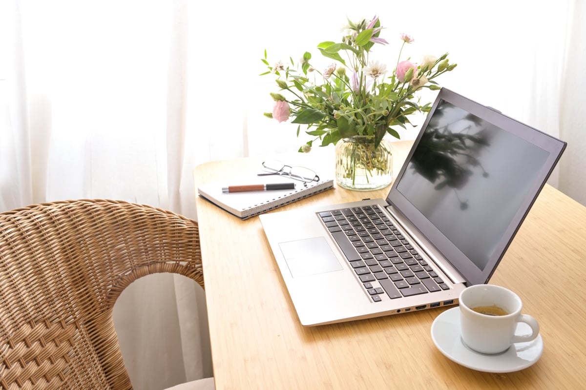 Laptop computer, coffee, and stationery on a wooden table in a cozy home office